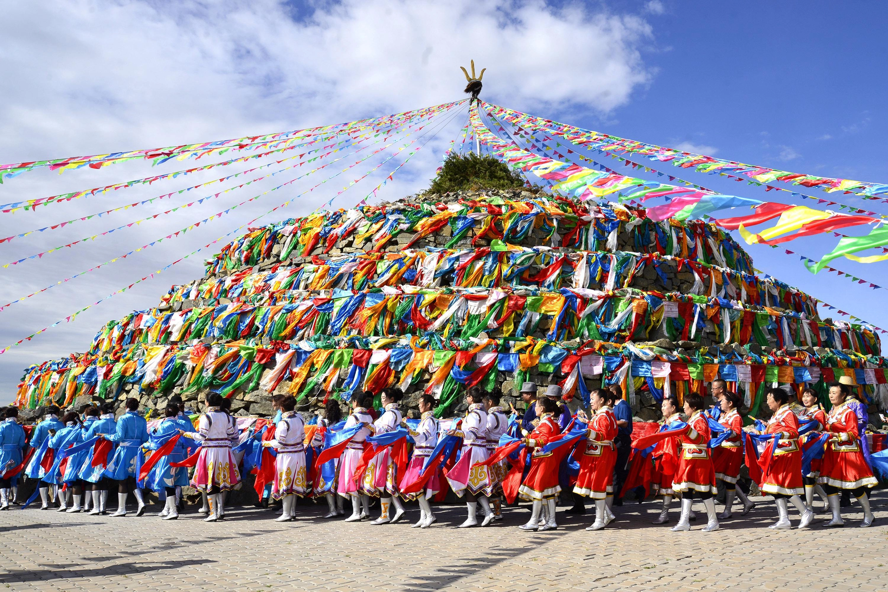 Mongolian herders performing traditional oboo worship ceremony with stone cairn and colorful prayer flags