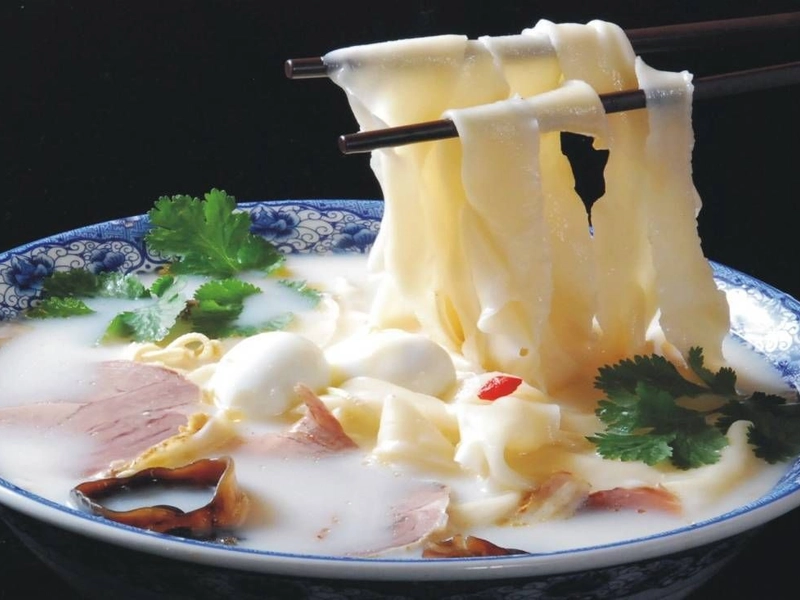Steaming bowl of Henan Huimian noodles with lamb and herbs in rich broth