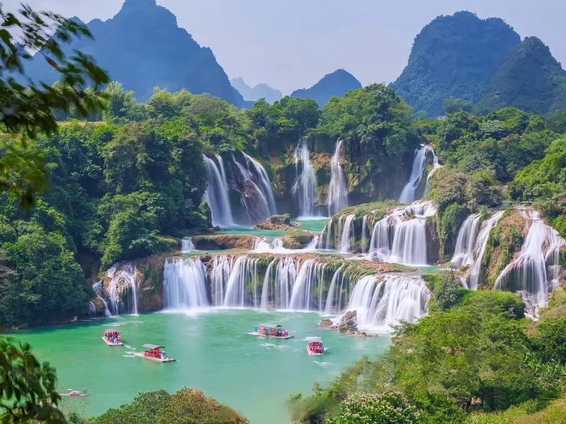 Detian Waterfall on the China-Vietnam border, water cascading over cliffs with mist rising, surrounded by lush vegetation