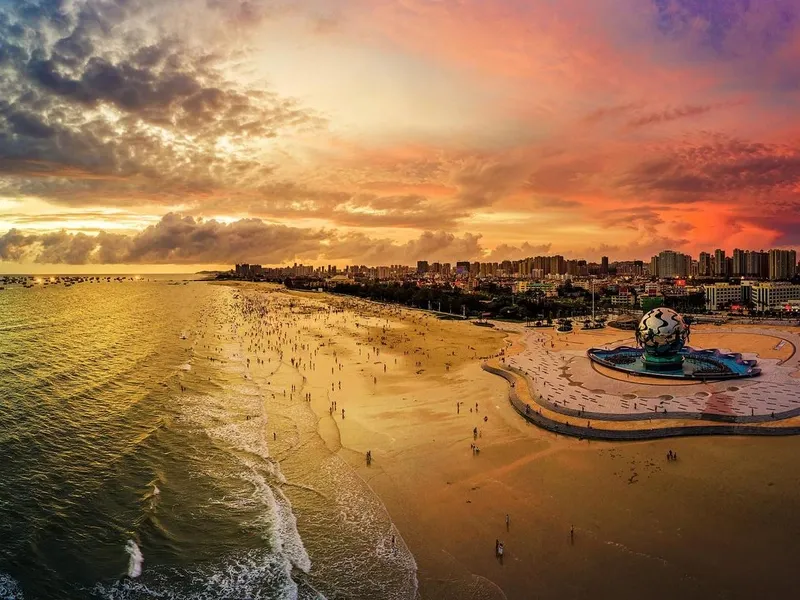 Beihai Silver Beach with silvery sand and clear blue waters, visitors walking along the shore and palm trees swaying