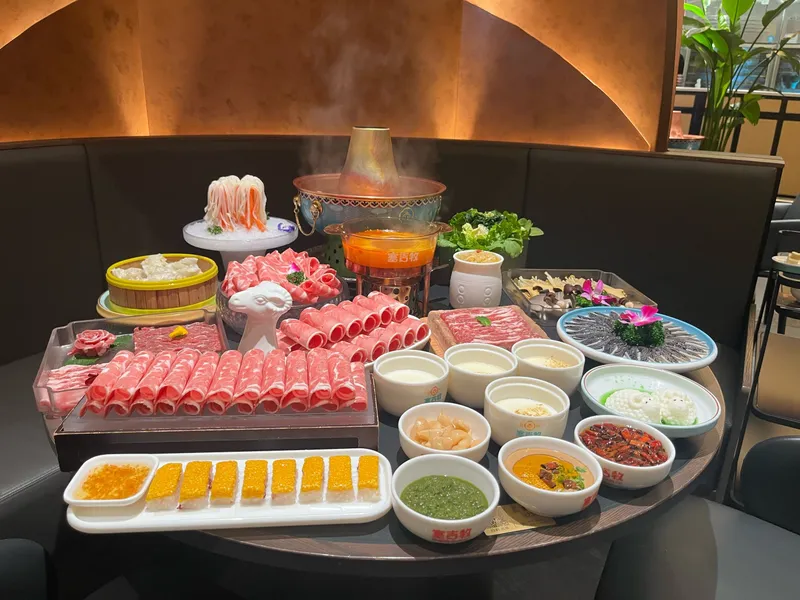 Communal hot pot with sliced meats, vegetables, and seafood