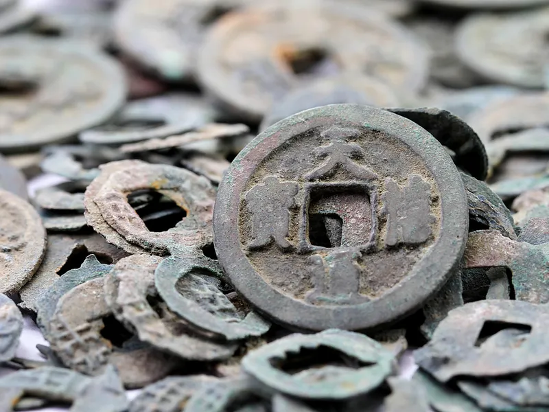 Illustration of ancient Chinese money including cowrie shells, bronze spade and knife coins, round coins with square holes, and Song dynasty paper currency, showing the evolution of Chinese monetary history.