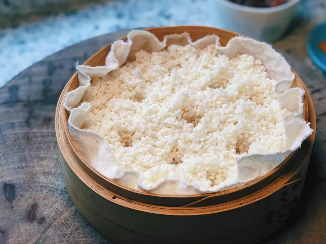 Sticky rice being steamed in a bamboo steamer, the preferred method for achieving perfect chewy texture