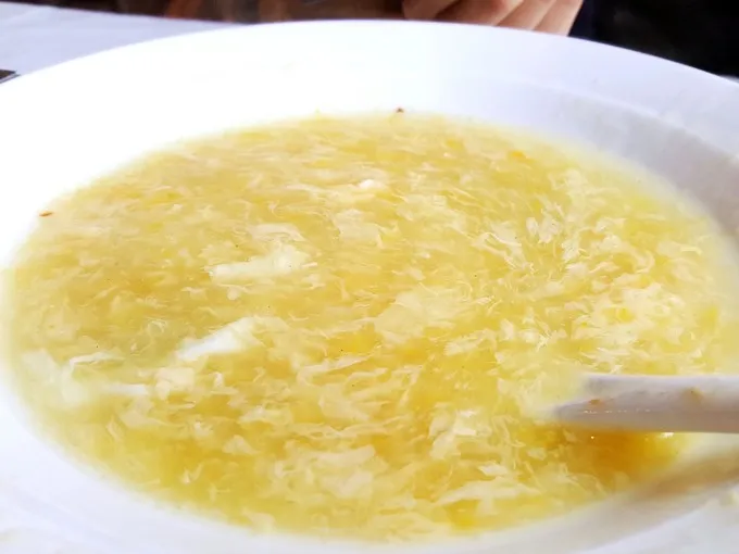 A steaming bowl of egg drop soup with delicate egg ribbons floating in clear broth, garnished with scallions, showcasing a classic and comforting Chinese dish.
